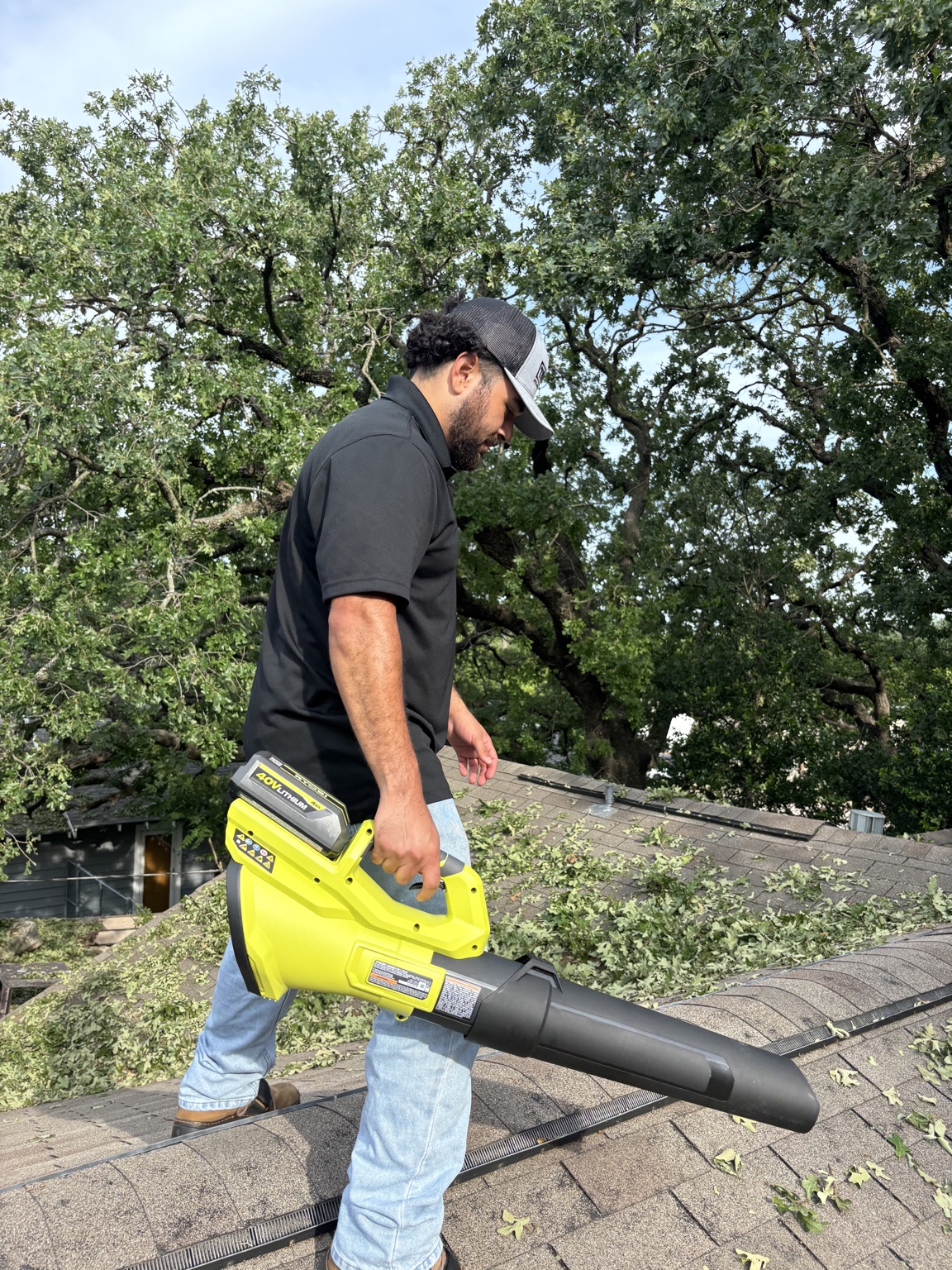 Worker clearing storm debris from a roof with a leaf blower