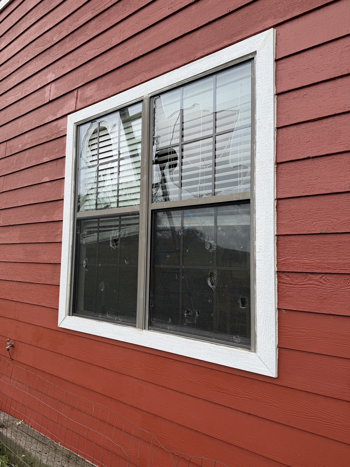 Broken window with damaged glass on a red-sided exterior wall